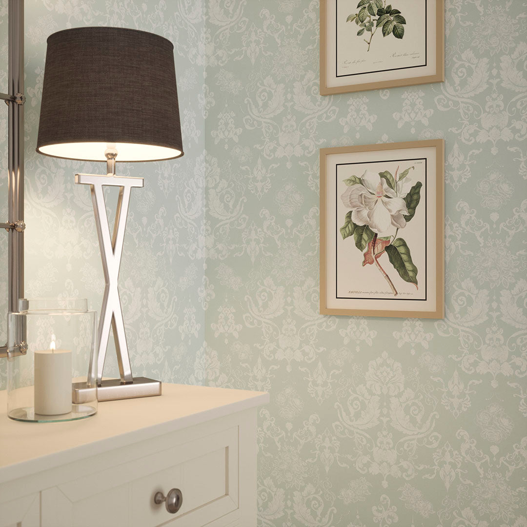 Hallway nook with a white table, lamp and floral artwork on a wall. Walls feature damask wallpaper in mint green.