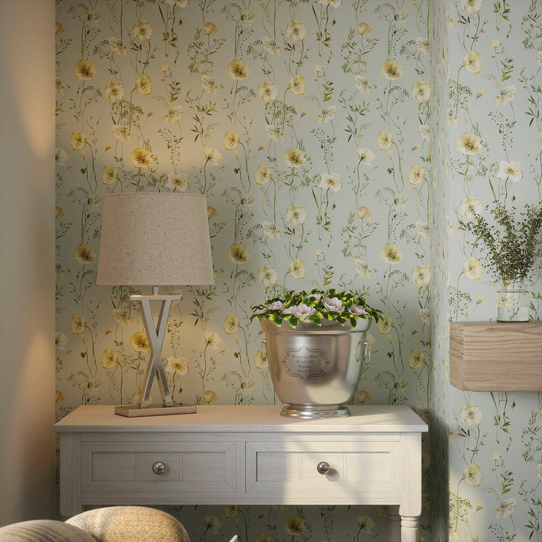 Living room nook with lamp and metallic vase on a wooden table, set against seafoam green wallpaper featuring cream florals.