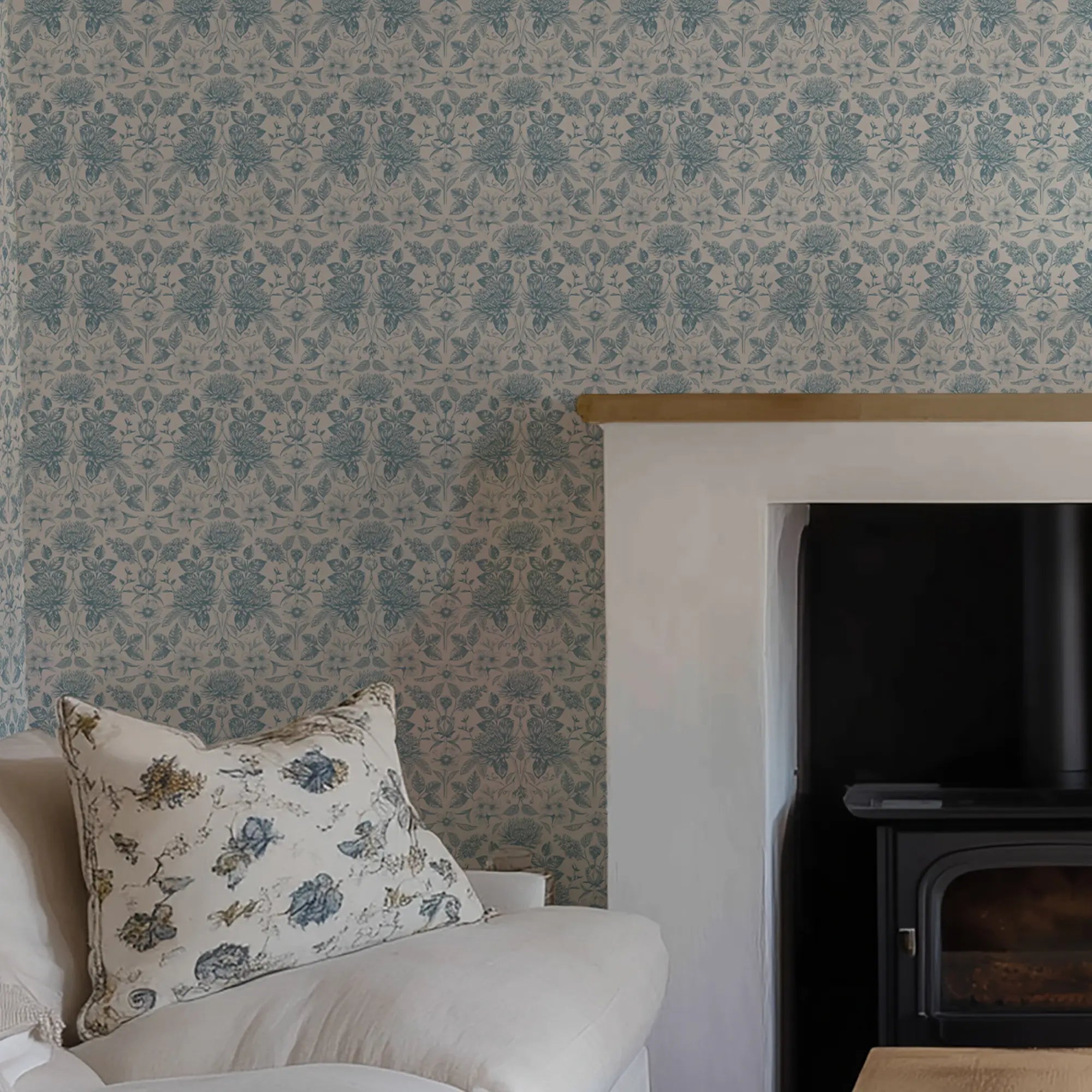 Floral-patterned pillow on a sofa against a decorative wall with blue floral wallpaper, with a fireplace.
