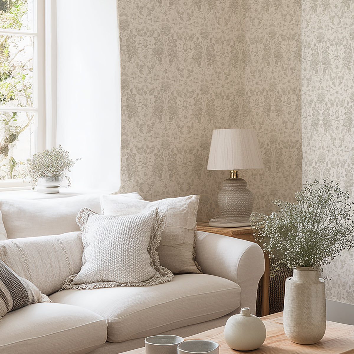 Living room with beige sofa and floral wallpaper, decorative pillows, and a lamp on a side table.