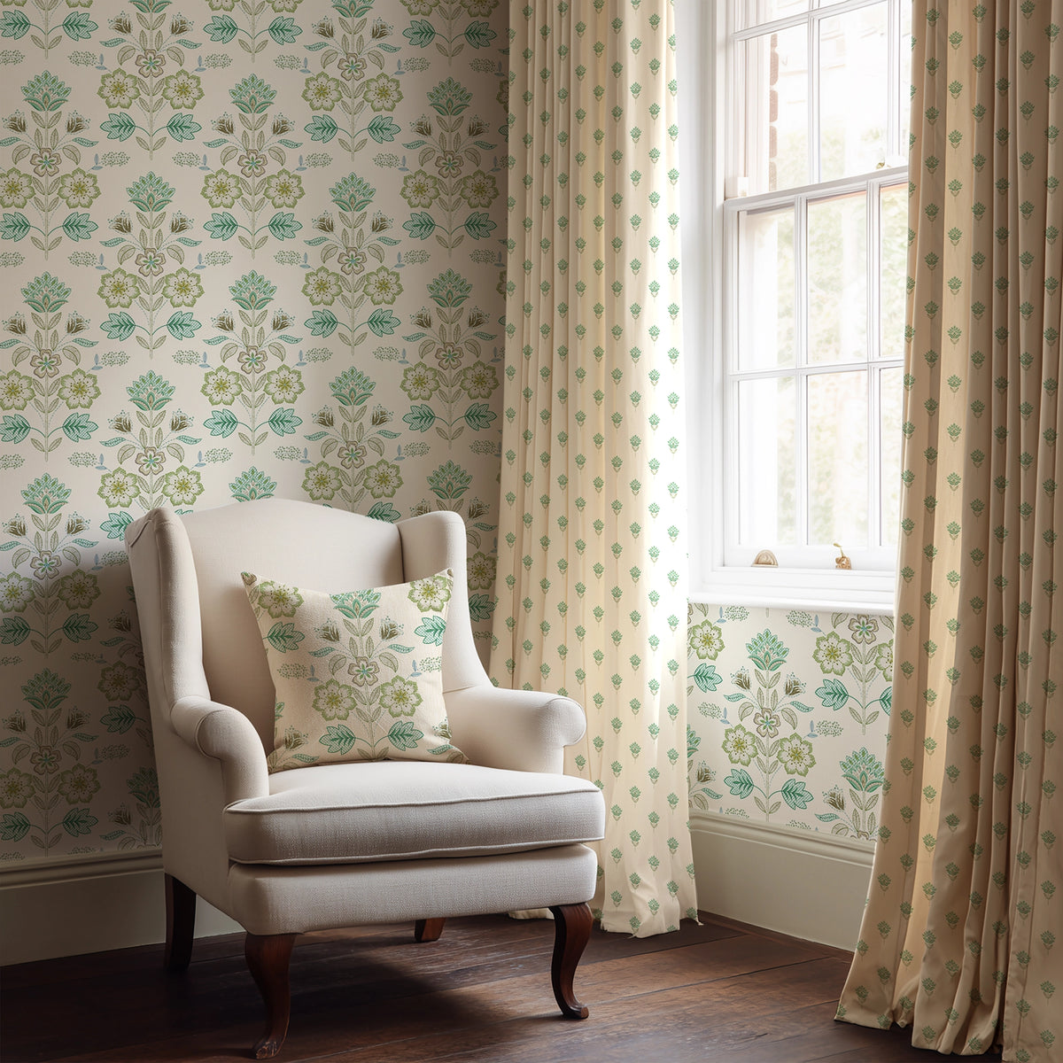 Beige armchair with a patterned pillow in a room with green floral wallpaper and matching curtains.