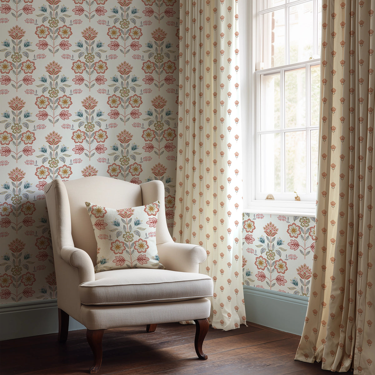 Beige armchair with floral pillow in a room with floral-patterned wallpaper and curtains.