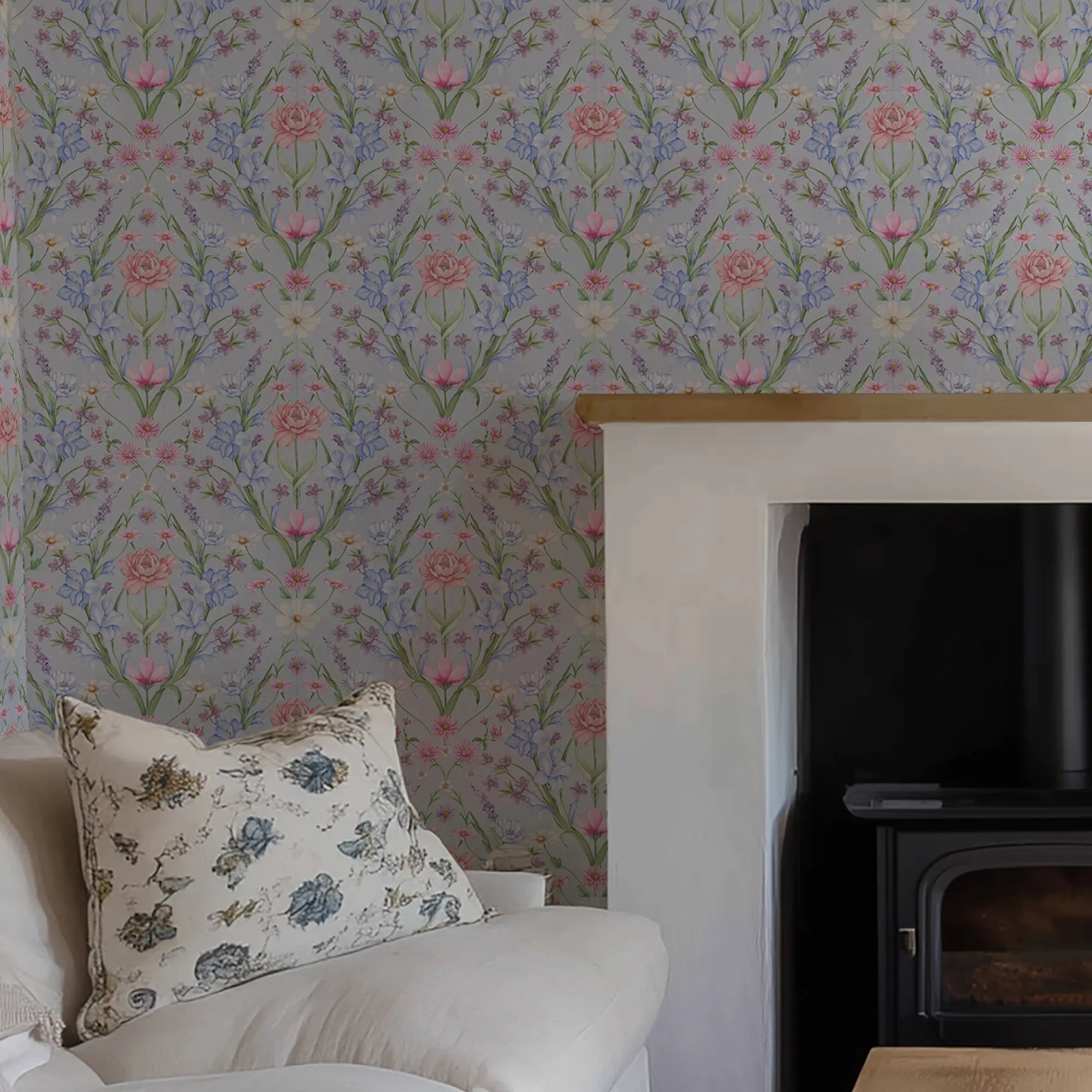 Large scale, floral-patterned wallpaper with a white fireplace and a floral pillow on a chair.