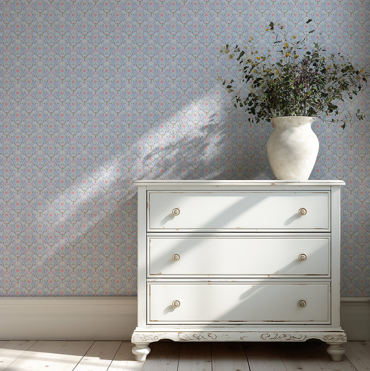 White dresser with a vase of flowers against a light blue, floral-patterned wall.
