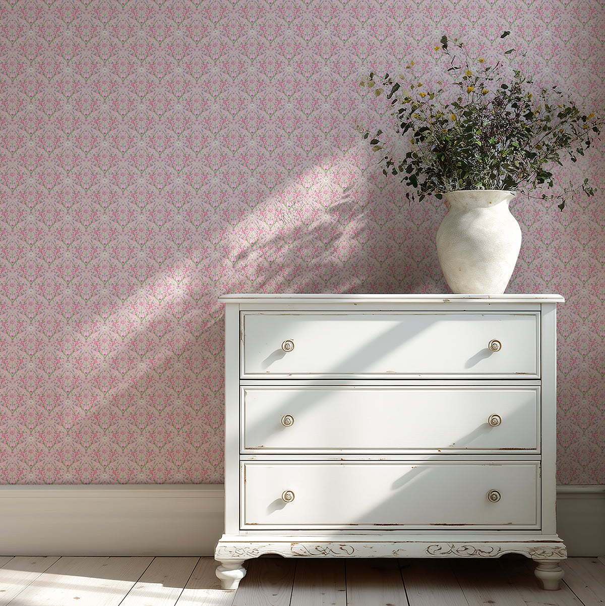 White dresser with a vase of flowers against a pink, floral wallpapered wall.