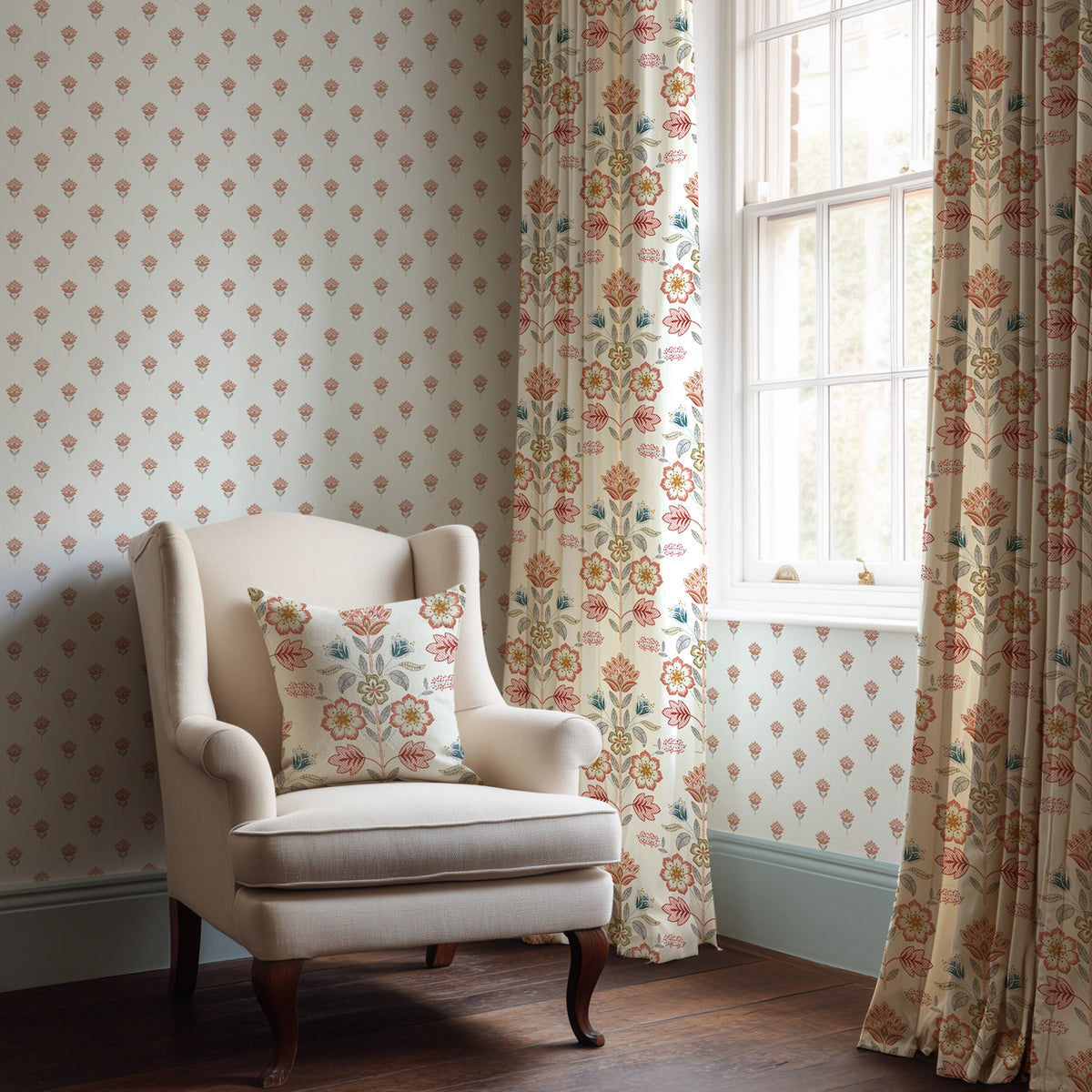 White armchair with floral pillow in a room with floral-patterned wallpaper and curtains.