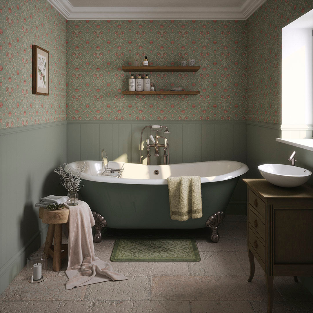 Cottage bathroom setting with green panelled walls, bathtub, free standing sink, and green wallpaper featuring repeated pink tulips and green foliage. 